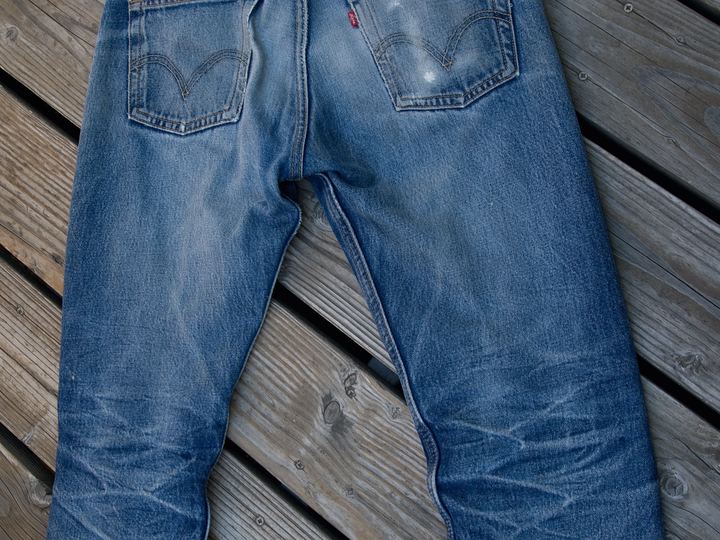 A pair of faded blue Levi's 501 jeans laid flat on a wooden deck, seen from the back with the leather patch at the waist