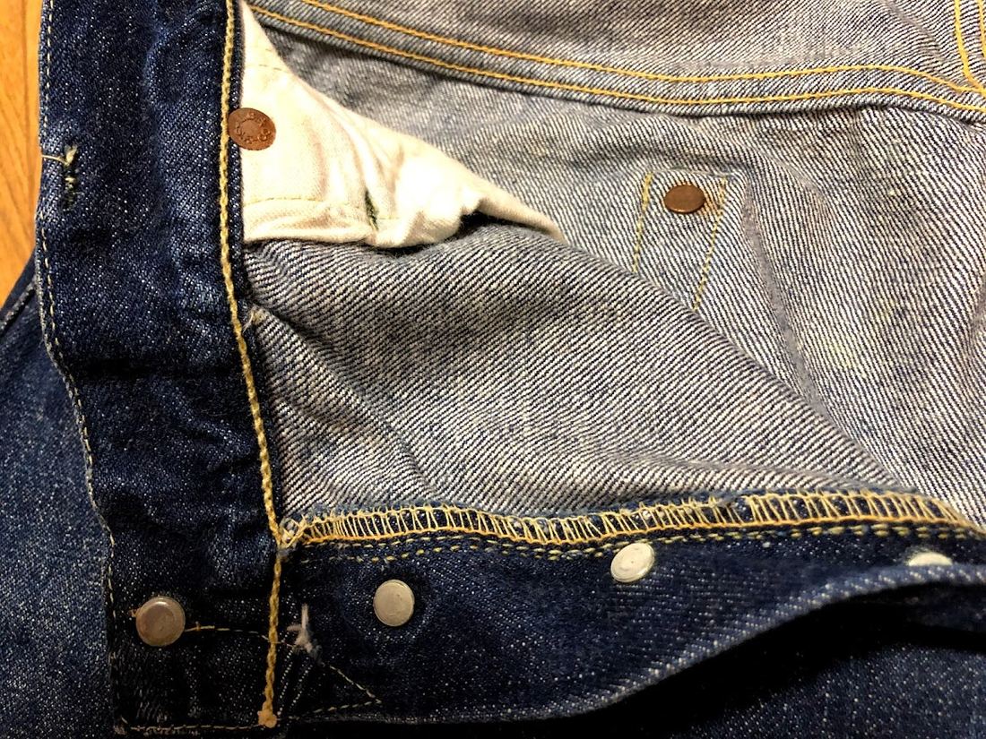 Close-up of the inside of a pair of dark denim jeans showing small copper rivets at the pocket corners
