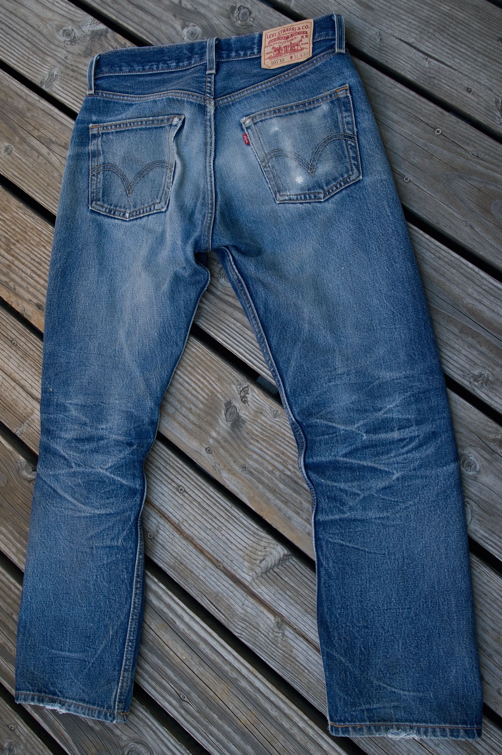 A pair of faded blue Levi's 501 jeans laid flat on a wooden deck, seen from the back with the leather patch at the waist