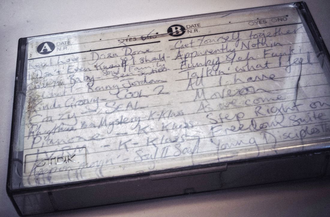 A clear cassette case with a handwritten track list for sides A and B of a homemade mixtape