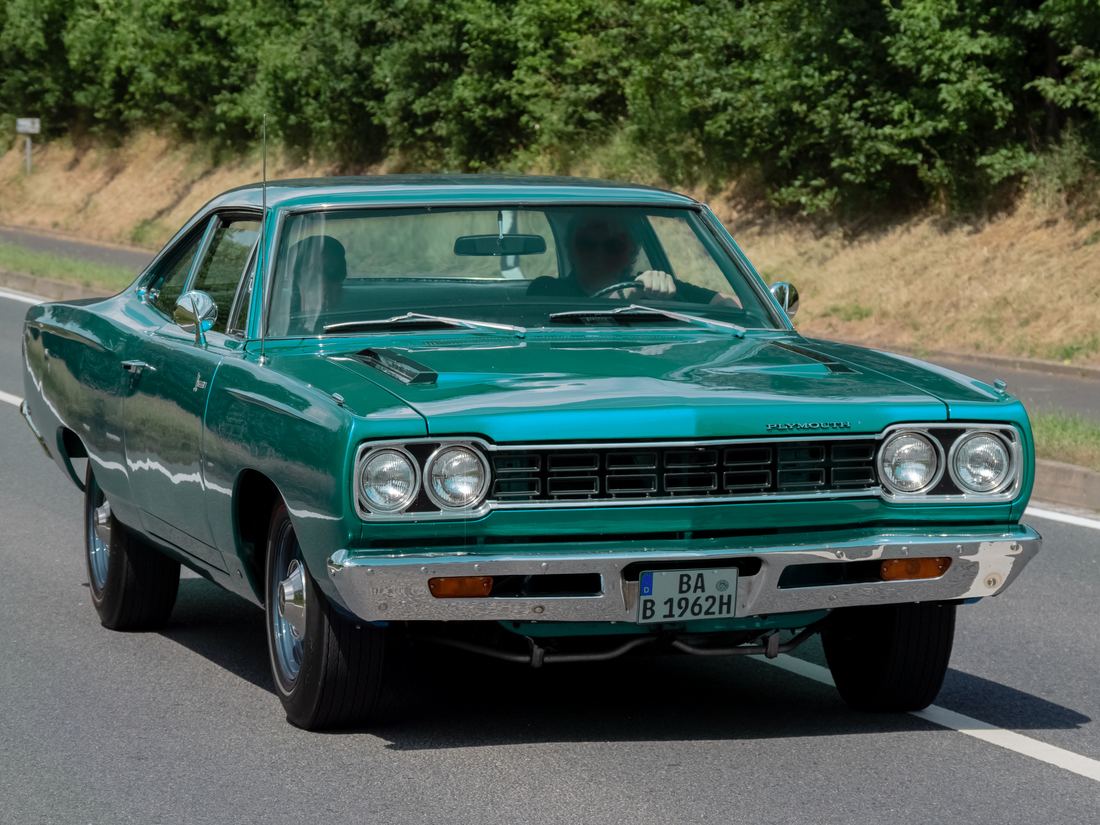 A green 1969 Plymouth Road Runner with a black hood stripe driving along a country road
