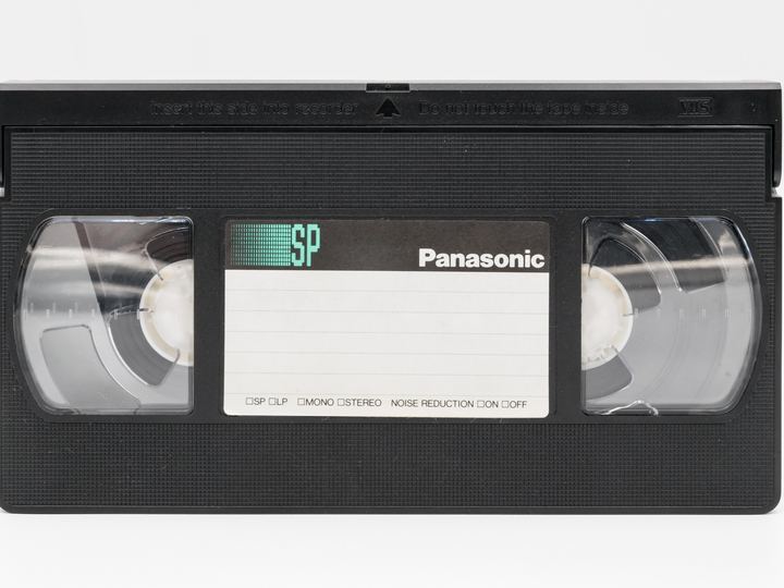 A black VHS videocassette with clear reel windows and a white label area, on a white background